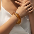 Retro geometric amber acrylic bangle featuring marbled resin textures on a model's wrist - Random Pattern / Caramel Amber (AB0044-1)