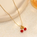 Elegante collar dorado con colgante de cereza y cuentas rojas sobre un fondo texturizado - Cereza