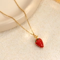 Collar de cadena dorada de moda con un dije de fresa roja sobre una superficie blanca - Fresa