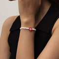 Detalle de pulsera de cuentas blancas con flor roja y un dije con la letra A grabada - Blanco/Rojo / Pulsera