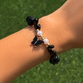 Dettaglio della collana con pietre nere, perle e ciondolo a farfalla sull'erba verde - Bracciale / Nero