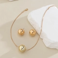 Detailed view of polished gold ball pendant necklace and matching stud earrings on rock - Earrings And Necklace / Gold