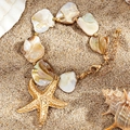 Detail view of shell bracelet with gold starfish charm on beach sand texture - White Bracelet(2494)
