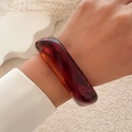 Detailed view of a wide amber resin bracelet with vintage marble texture on a model's wrist - Brown (2503)