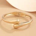 Polished gold irregular teardrop bangle with spring hinge closure on a beige background - Wrap Around Teardrop Hinged Style (2426)