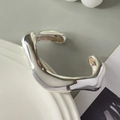 Detail of silver wavy open cuff bracelet with irregular fluid design on ceramic plate - Irregular Wave (2267) / Silver