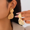 Macro detail of gold fan-shaped earrings with textured pleats on a fashion model - Gold Style (3514)