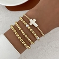 Detail eines vierteiligen goldenen Perlenarmband-Sets mit Kreuzanhänger und Perle am Handgelenk - Gold Ton Marmormuster Kreuz Stil (6317)