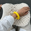 Detail van een heldergele brede hars armband gedragen op een witte geweven tas - Geel