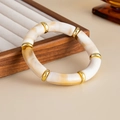 Detailed close-up of acrylic bamboo-style stretch bracelet with marble texture and gold rings - Off White