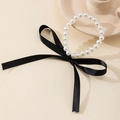 Detailed view of white pearls with a large black velvet ribbon bow on a cream background - Bracelet / Black Bracelet