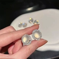 Boucles d'oreilles ovales avec pierre translucide et halo de zircons montrées à la main - Style Halo Ovale Pierre de Lune / Argent