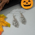 Detailed close-up of gothic silver skeleton hand earrings with festive Halloween decor - Silver Skeleton Hand Ear Hook