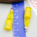 Close-up of yellow resin soda bottle charms measuring 4cm with ruler for size reference - Small Bottle Style (24643) / Transparent Yellow