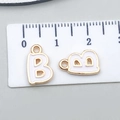 Detail view of a white enamel letter B pendant with gold edging and a ruler for size reference - Letter B