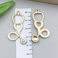 Détails recto-verso de pendentifs stéthoscope dorés avec émail blanc et strass pour DIY - Stéthoscope Émail Blanc 43x23mm (23231)