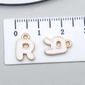 White enamel letter R charm with gold trim and top loop measured on a metric ruler - Letter R