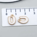 Letter U white enamel charm with gold metal frame on a ruler for size reference - Letter U