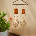 Detail of leaf earrings with brown leather texture and golden twisted metal rings on a stand - Brown
