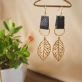 Leaf charm earrings with black leather and golden rings on a creative display - Black