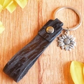 Détail du pendentif tournesol sur porte-clés en cuir noir sur bois avec des pétales jaunes - Motif Litchi Noir (3)