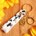 Detail of cow print leather keychain with gold sunflower charm on wood background - Gold Cow Pattern