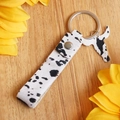 Detail of cow print leather keychain with bull head charm on a wooden table with sunflowers - Cow Pattern Style