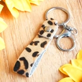Dettaglio portachiavi in pelle leopardata con finiture in argento su superficie di legno - Stile Leopardo 1