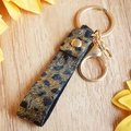 Dettaglio del portachiavi in pelle con stampa leopardata, paillettes oro e moschettone - Stile Leopardato Nero e Oro