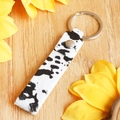 Dettaglio portachiavi in pelle con stampa mucca e anello argento su sfondo di legno - Stile Stampa Muccata (4838918343669)