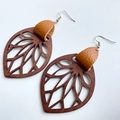 Macro detail of leaf-shaped earrings featuring cutout wood and brown textured leather - Brown