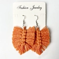 Detailed close-up of handmade bohemian orange fringe earrings with woven cotton leaf texture - Warm Orange