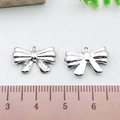 Detailed view of silver bow-shaped alloy pendants measured with a ruler for scale - Small Bowknot (21385)