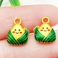 Detail van twee mini Zongzi-bedeltjes in de hand tonen klein formaat en vergulding - Groene Emaille Zongzi (22229)