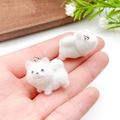 Handheld view of two white flocked puppy charms for DIY jewelry and accessories - Samoyed (23141) / White Pink