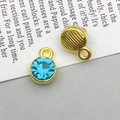 Detail of round gold-plated charms with sky blue crystals and striped texture backings - June - Light Blue