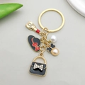 Gouden sleutelhanger met zwarte emaille hoed, lippenstift en parelhangers in detail - Dames Mode Combinatie Stijl (ER596)