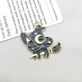 Detail showing a black enamel wizard cat pendant with golden metal outlines on a flat surface - Black Cat Riding a Broomstick (18137)