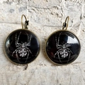 Detail view of gothic lever-back earrings featuring a white spider motif on glass cabochon - White Spider Totem (3) / Bronze
