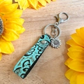 Détail du porte-clés vintage en cuir avec pendentif tournesol sur un fond en bois - Style Pendentif Métal Tournesol (3)