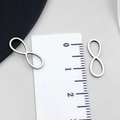 Macro view of silver infinity charms showing 20mm length measurement on a ruler - Infinity Symbol Style