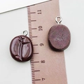 Pendenti ovali in resina viola scuro con passante in metallo accanto a un righello marrone - Caffè Resina Chicco di Caffè (24108)
