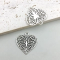 Primer plano macro de dos colgantes de corazón plateados vintage con diseño de mariposa - Mariposa Calada Corazón Plata Antigua (16475) / 22x22mm