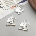 Macro view of three silver alloy graduation cap and diploma charms for DIY jewelry making - Bright Silver