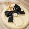 Close-up of a large black satin bow keychain with white pearls on a ceramic plate - Black Bow (ZJ15864)