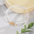 Detail of white braided bracelet with gold U-shaped link on a ceramic tray - White