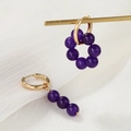 Detailansicht asymmetrischer Goldohrringe mit lila Perlen auf weißem Plissee-Stoff - Violette Perle (ZJ6533)