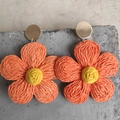 Macro view of woven raffia flower earrings in bright orange and yellow on a grey stone - Orange