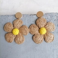 Detailed close-up of woven raffia flower earrings with yellow centers on stone - Natural Wood Color