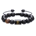 Detalle de una pulsera de ónix negro de 10 mm con letra E dorada y ojo de tigre - Letra E